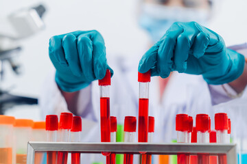 A scientist examines samples with a microscope in a laboratory with test tubes filled with colorful...
