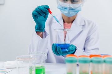 A scientist examines samples with a microscope in a laboratory with test tubes filled with colorful liquids in the background.