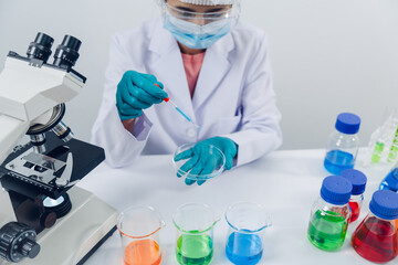 Fototapeta premium A scientist examines samples with a microscope in a laboratory with test tubes filled with colorful liquids in the background.