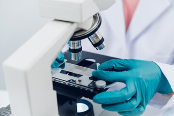 A scientist examines samples with a microscope in a laboratory with test tubes filled with colorful...