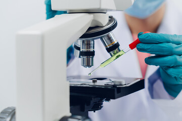 A scientist examines samples with a microscope in a laboratory with test tubes filled with colorful...