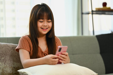 Happy asian child girl watching children content in social networks on mobile phone