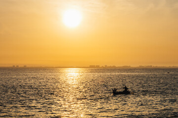 Landscape shot of two hardworking men rowing boat during sunrise under bright sun and a calm sea....