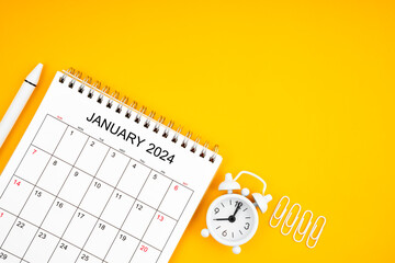 Fototapeta na wymiar January 2024, Monthly desk calendar for 2024 year and alarm clock with paper clips on yellow color background.