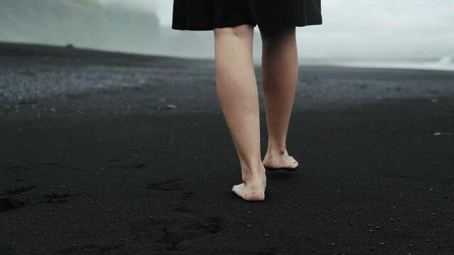 Feet walking on black sand beach, Iceland, beautiful woman in black dress, slow motion tracking, dramatic seascape