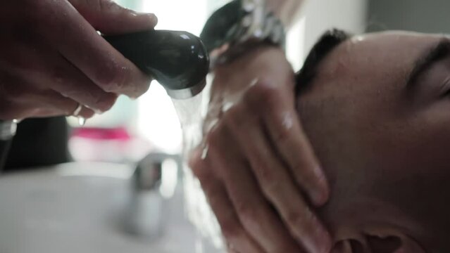 A master in a barbershop washes the hair of a male client with shampoo and water after a haircut. Modern and fashionable haircut. Slow motion