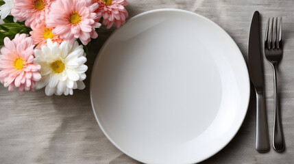 A top-down view of a white plate with pink flower alongside a fork and knife on a textured gray surface
 - Powered by Adobe