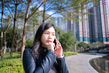 Beautiful woman with long hair in black leather jacket using mobile phone on the park