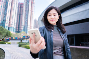 Woman with long hair in black leather jacket using smartphone video chat with friend