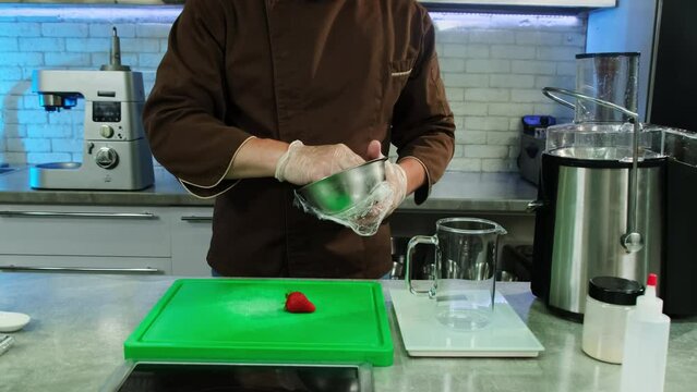 Culinarian takes strawberries out of bowl and puts on carving board. Scene complimented by professional kitchen equipment surrounding