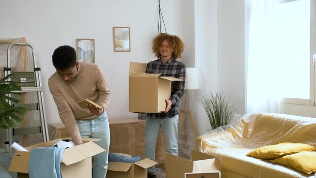 Two men packing in a moving cardboard box to settle in a new home. Student residence relocation.