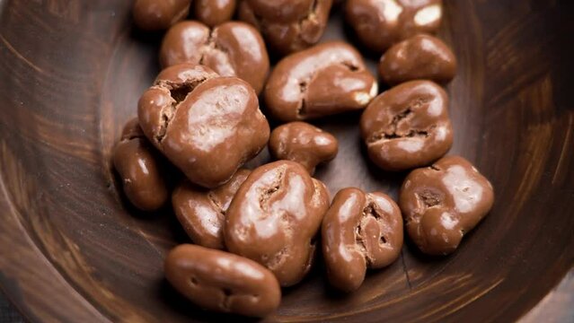 Chocolate covered walnut. Delicious nutritious nut candies falling into a rotating wooden bowl close up. Slow motion