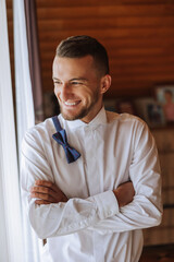 A stylish portrait of the groom preparing for the wedding ceremony in the morning. Groom's morning. Preparation for the groom's morning. The groom puts on a jacket. The confident look of a mature man.