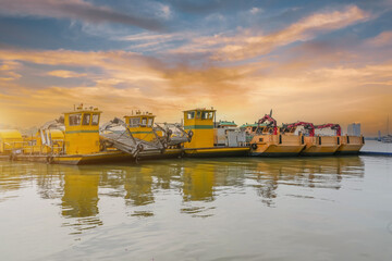 Small several row of ships with a claw manipulator hand parked at the port pier at sunset sky