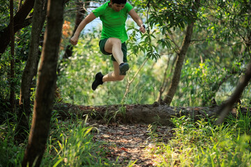 Woman trail runner jumping over a fallen tree trunk in tropical forest