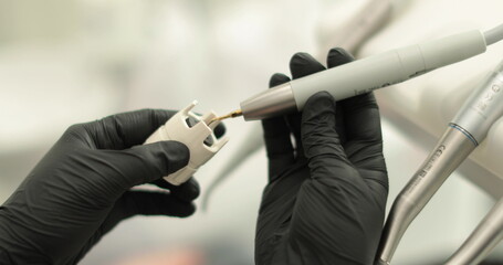 The hands of a female dentist are holding a drill in their hands. Close-up of a dental drill in the...