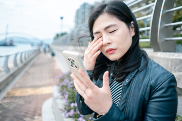 Asian woman rubbing her tired eyes when using smartphone.