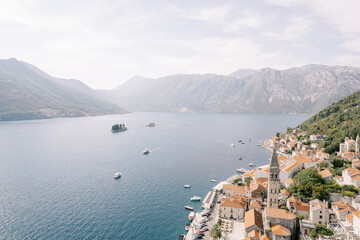 Fototapeta na wymiar Shore of Perast with a high bell tower among ancient houses overlooking the islands of the Bay of Kotor. Montenegro. Drone