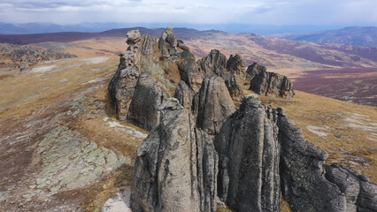 Fototapeta premium Mysterious fabulous tower rock formations of hill mountain in overcast weather. Black raven dark forces is flying in prairie wild nature. Range stone remnants buttes. Aerial view in national park