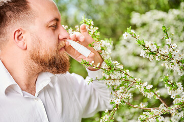 Man allergic using medical nasal drops, suffering from seasonal allergy at spring in blossoming...