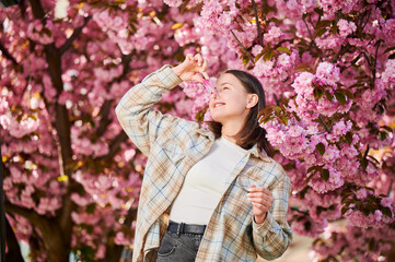 Woman allergic suffering from seasonal allergy at spring. Smiling woman with clothespin clipped to his nose - symbolic gesture of his inability to breathe due to nasal congestion near blooming tree. - obrazy, fototapety, plakaty