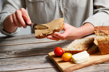 close up woman hands spreading pate on a piece of seed bread over a wooden table