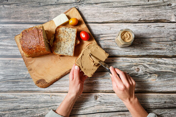 close up woman hands spreading pate on a piece of seed bread over a wooden table