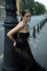 A 30-year-old girl in a black transparent revealing dress on a city street. Style and elegance, femme fatale, photo shoot, advertising, girl 