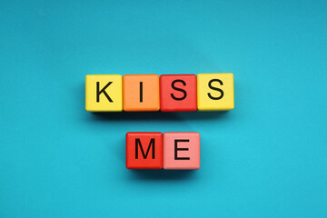 Colorful cubes with phrase Kiss Me on light blue background, flat lay