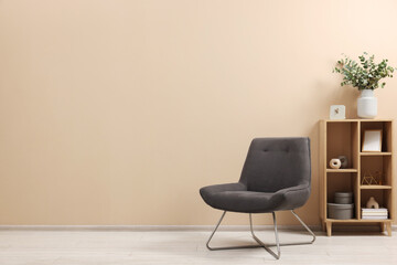 Living room interior with comfortable armchair and shelving unit near beige wall indoors. Space for text