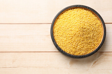 Millet groats in bowl on light wooden table, top view. Space for text