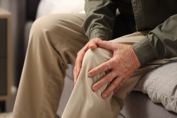Senior man suffering from knee pain indoors, closeup. Rheumatism symptom