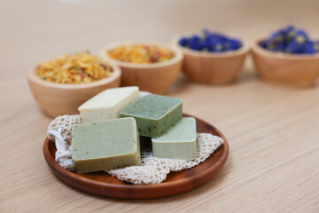 Tray with soap bars and bowls of dry flowers on light wooden table. Spa therapy
