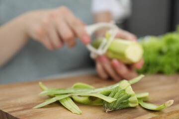 Woman peeling fresh zucchini at table, focus on peels