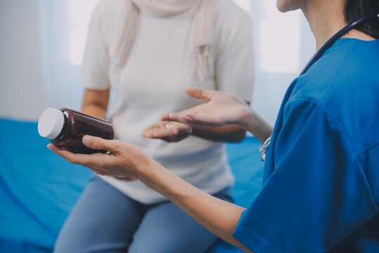 Asian Woman Nurse Holding A Medicine Bottle And Telling Information To Asian Senior Woman Before Administering Medication. Caregiver Visit At Home. Home Health Care And Nursing Home Concept.