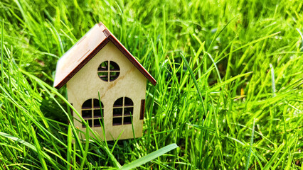 miniature toy house in grass close up, spring natural background. symbol of family. mortgage, construction, rental, property concept. Eco Friendly home. Blurred and selective focus