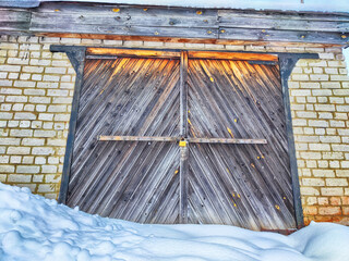 Old wooden gate in brick garage and white snow. Background, texture, location