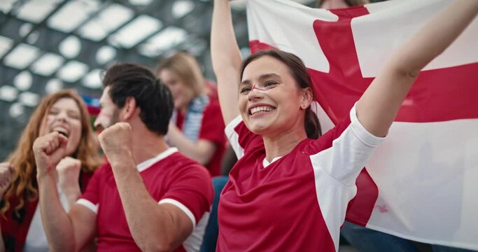 Cheerful fans supporting their team on day of important match. People having painted face cheering footballers while sitting in stands. Cute woman with flag of England happy from successful game.