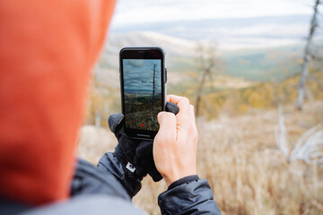 The guy takes pictures with his phone of the nature around, beautiful landscape, mobile photography in the mountains.