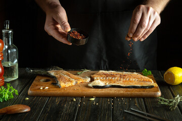 A cook adds spices to a trout steak in a restaurant kitchen. Pink salmon is a delicious fish for...
