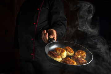 Professional chef prepares donuts in a frying pan. The concept of preparing a Ukrainian national dish in the kitchen. Dark space for advertising.