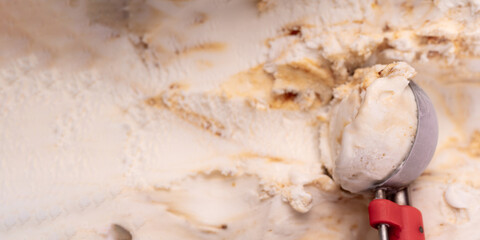 Stainless steel ice cream scoop is scooping caramel flavor ice cream, top view, close-up.