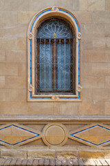 Mamluk archirtecture style single arched window framed by a rustic brick wall. The intricate...