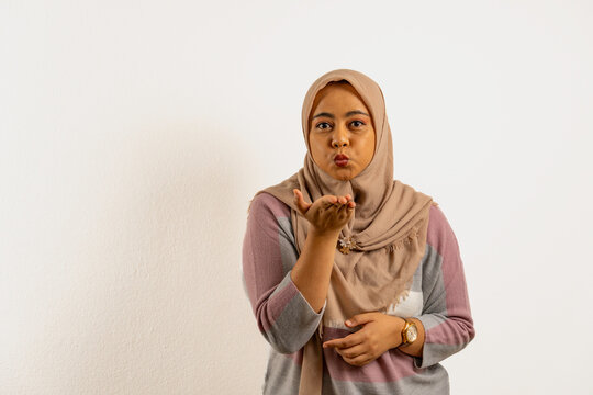 Asian Muslim woman wearing a hijab or headscarf blowing air kiss toward the camera. Indonesian woman on white background.