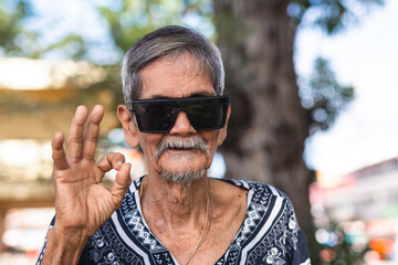 A cool hippie granddad saying its ok. Wearing shades and boho style shirt. Hanging out at the park. - obrazy, fototapety, plakaty