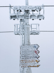 Frozen aluminium mast of a ski lift high up in the mountains with ice covered signs