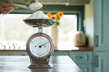 Woman's hand putting flour on an antique scale on the kitchen counter - obrazy, fototapety, plakaty