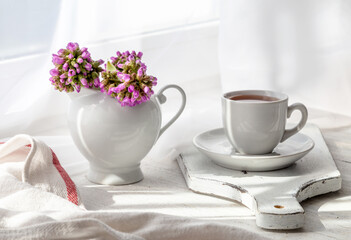 Spring still life with flowers in a vase and tea in a cup on the windowsill on a sunny day