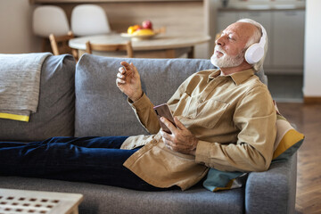 Time to relax. Joyful senior bearded man in wireless headphones listening to music, copy space,...