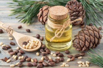 Cedar organic oil glass bottle, whole and shelled nuts on bamboo spoon, pine cones and green needle branches on wooden table.
